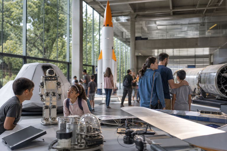 ITA promove evento gratuito com robôs, foguetes e simulador de avião em São José dos Campos Visitantes observam robôs, foguetes e projetos de engenharia em um espaço de divulgação científica