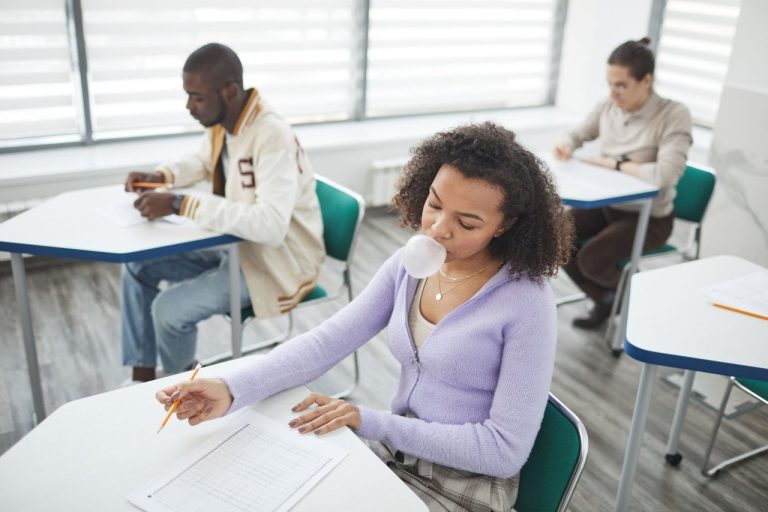 Grupo diverso de estudantes faz uma prova em uma sala de aula clara e moderna.