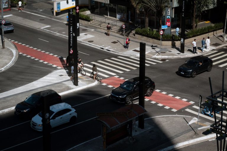 Mortes em vias urbanas caem 11,9% em São José dos Campos em 2026 Vista aérea de uma interseção urbana movimentada, com carros, ciclistas e pedestres circulando.